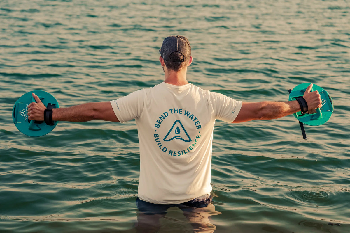 Man standing waist-deep in open water at sunset, arms outstretched, holding an Aqua-Bend disc in each hand
